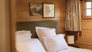 A cozy bed is placed by the wooden-finished wall with two portraits mounted above.