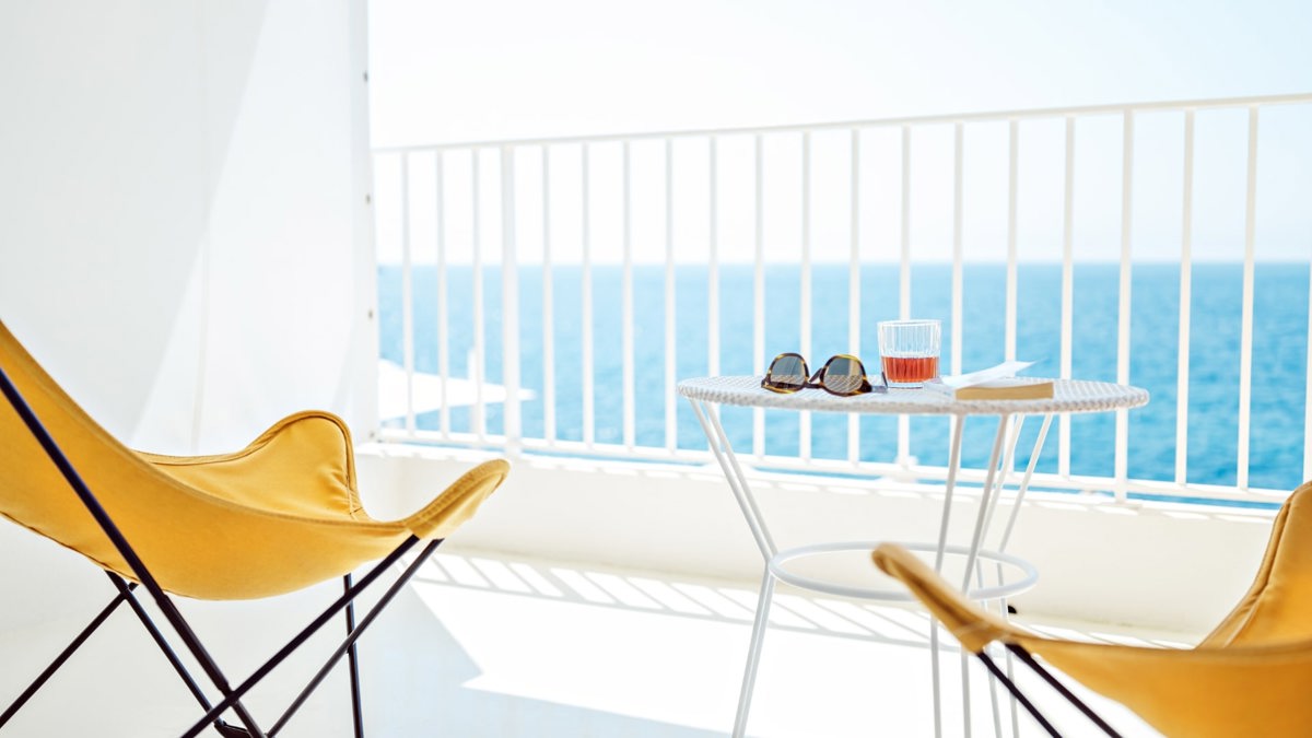 A wonderful ocean view is visible through the balcony glass, with two chairs and a table placed outside.