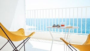 A wonderful ocean view is visible through the balcony glass, with two chairs and a table placed outside.