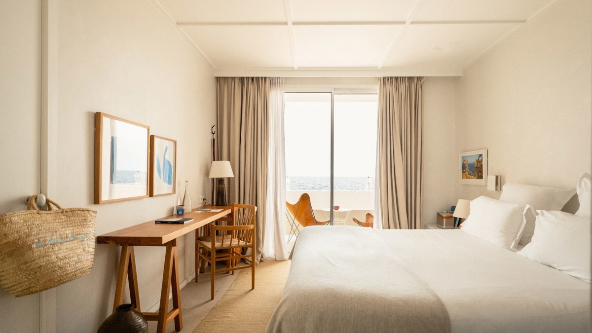 A well-organized bedroom features a cozy bed, a chair by the table, and a balcony offering a wonderful ocean view.
