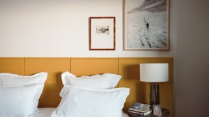 Two portraits are mounted above the bed’s side table, which holds a lamp.