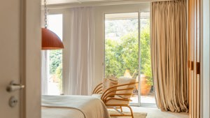 A wonderful view of the lush greenery outside is visible through the room’s glass door.