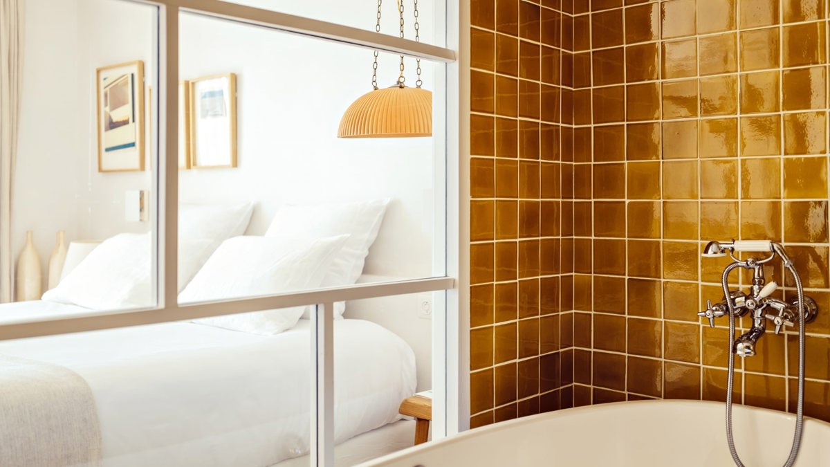 A well-organized bedroom is visible through the glass partition of the bathroom area.