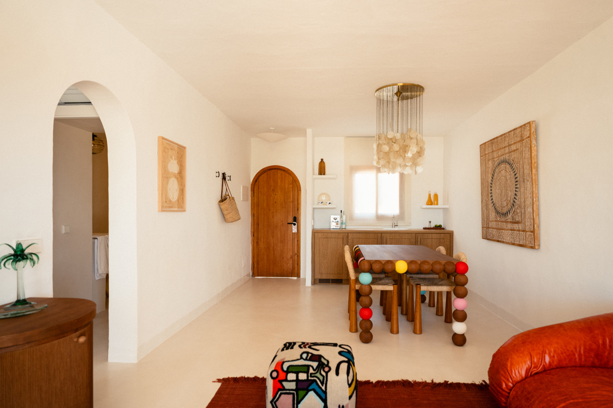 Espace de vie lumineux et éclectique avec table colorée, lustre en coquillages et canapé orange.