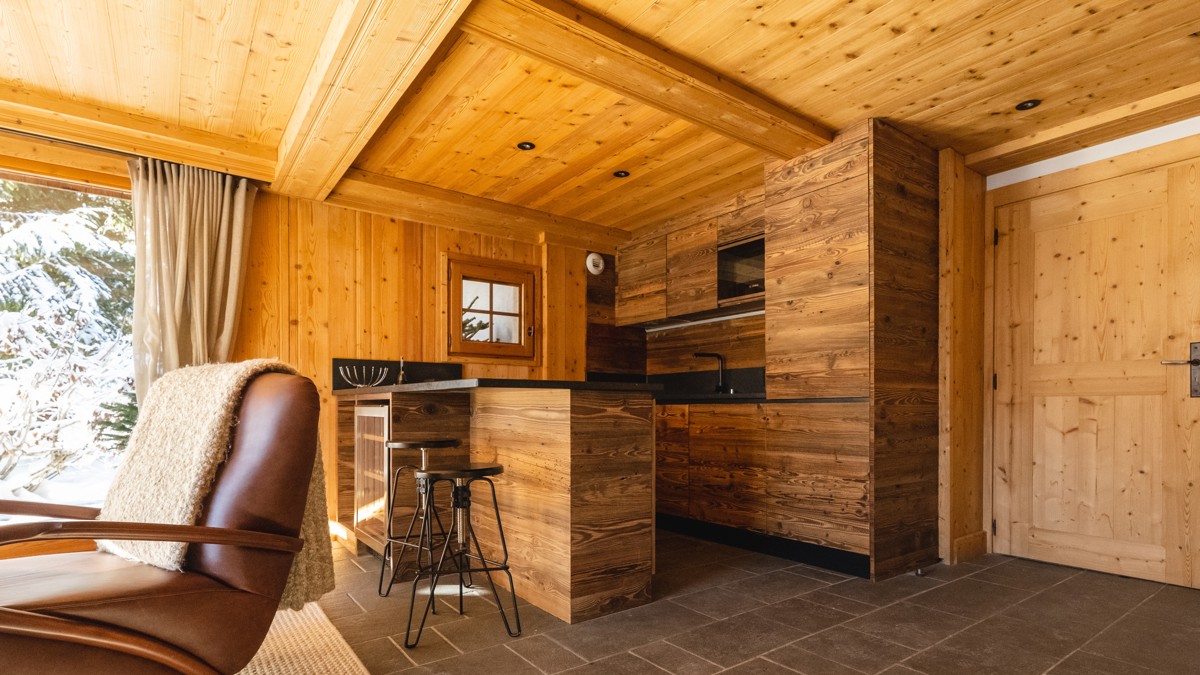 A clicked photo shows a wooden-finished empty kitchen and a cozy chair by snowy view.