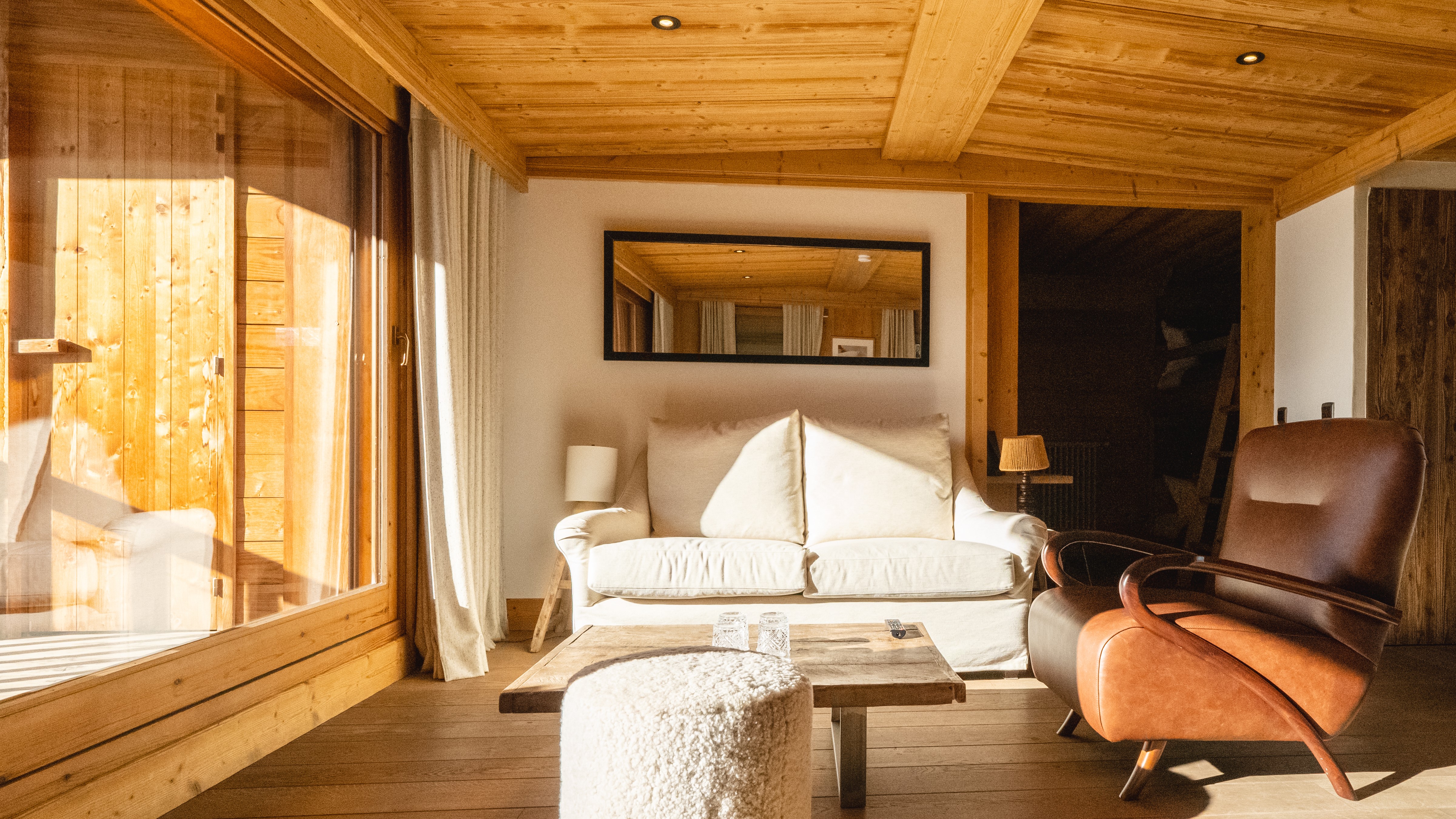 Living room with cream sofa, leather chair, and wooden decor, lit by natural light