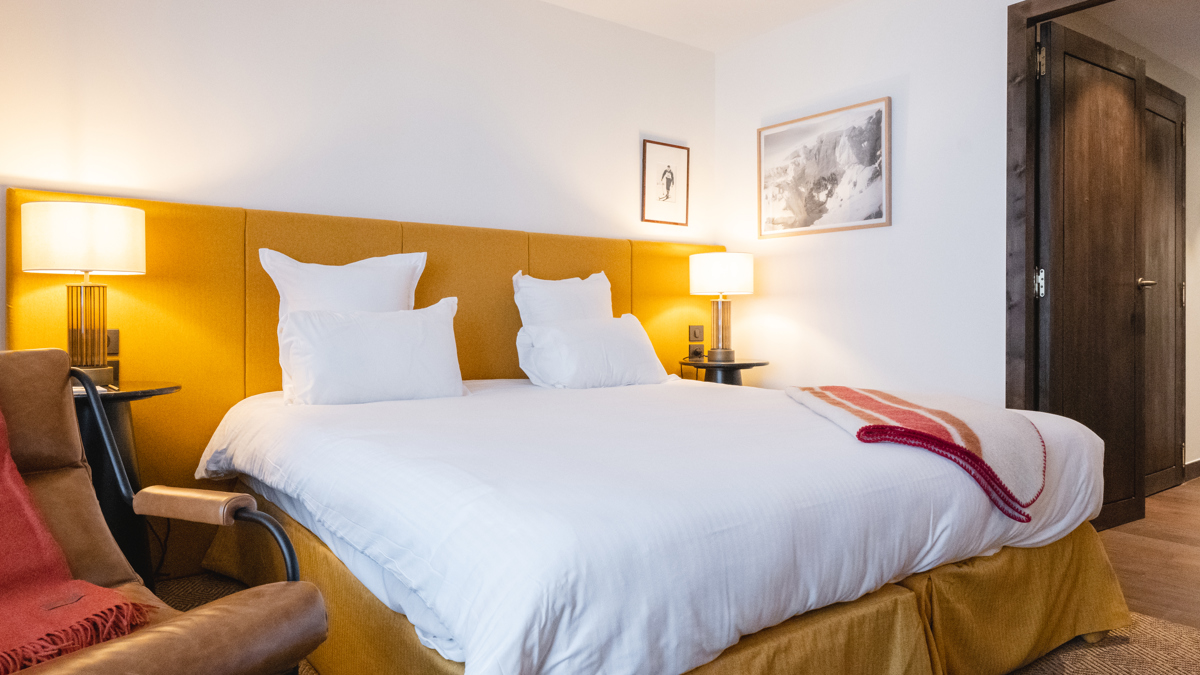 A bedroom features a cozy bed with two portraits above the side table and lamp.