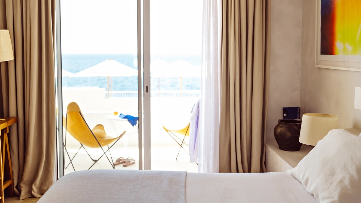 A well-organized bedroom features a cozy bed, portraits above, and a balcony with ocean view.