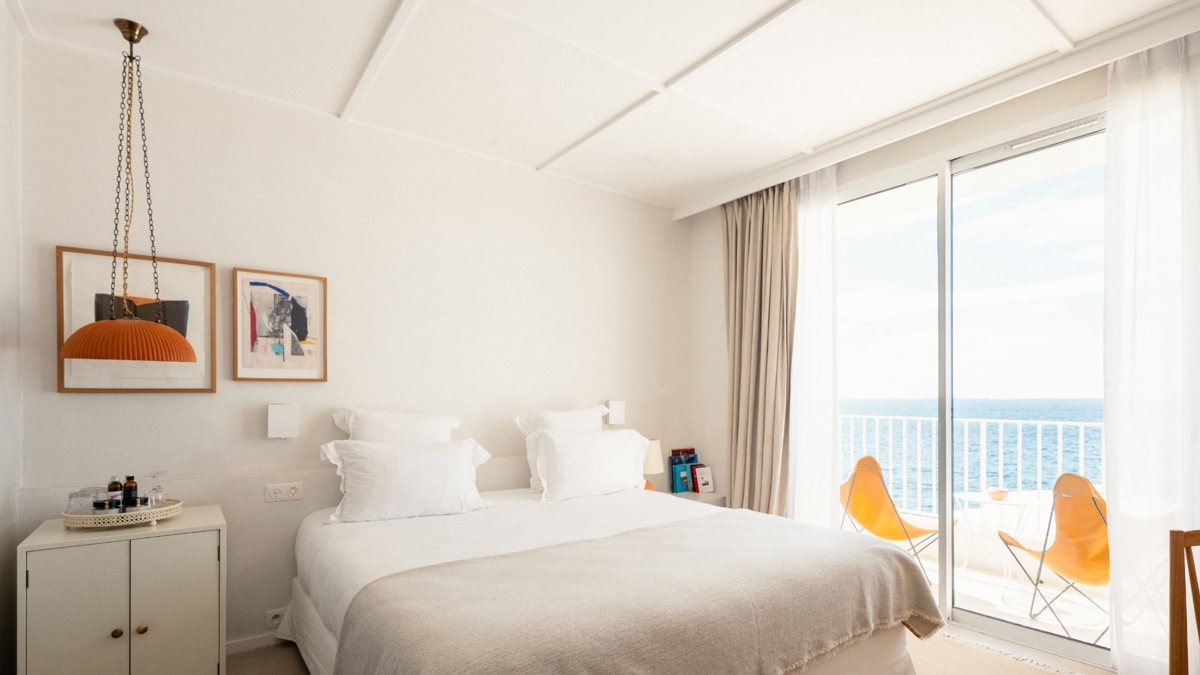 A well-organized bedroom features a cozy bed, portraits above the bed, and ocean-view balcony.