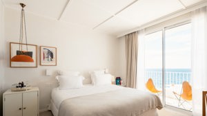 A well-organized bedroom features a cozy bed, portraits above the bed, and ocean-view balcony.