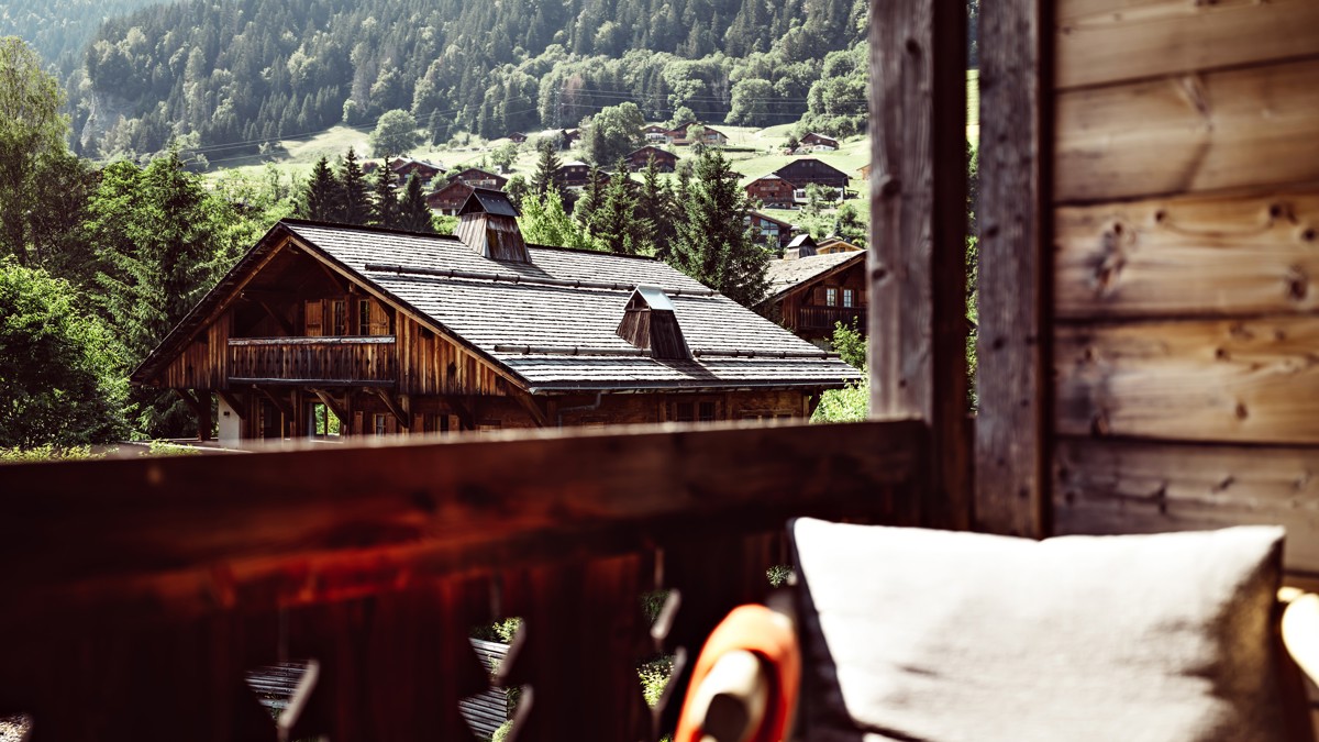 A view through arched windows reveals ornate architecture, green lawns, trees, and distant mountains.