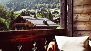 A view through arched windows reveals ornate architecture, green lawns, trees, and distant mountains.