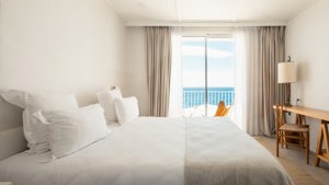 A well-organized bedroom features a cozy bed, chair by table, and ocean-view balcony.