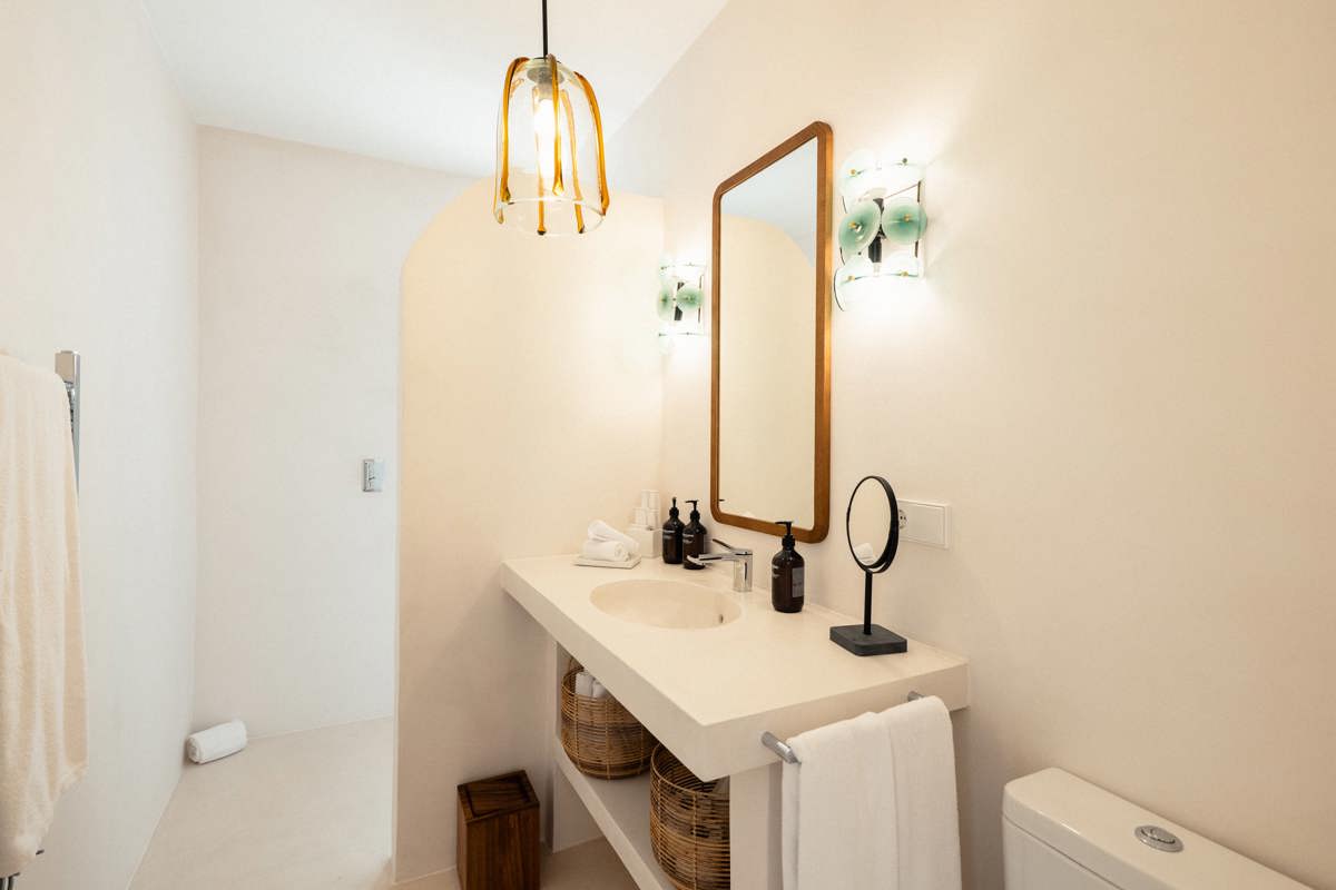 Salle de bain lumineuse avec un lavabo moderne, un miroir en bois, une suspension en verre, des paniers en osier et une décoration minimaliste dans des tons neutres.