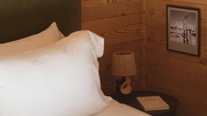 A lamp rests on the bedside table, with a portrait mounted on the wooden wall.