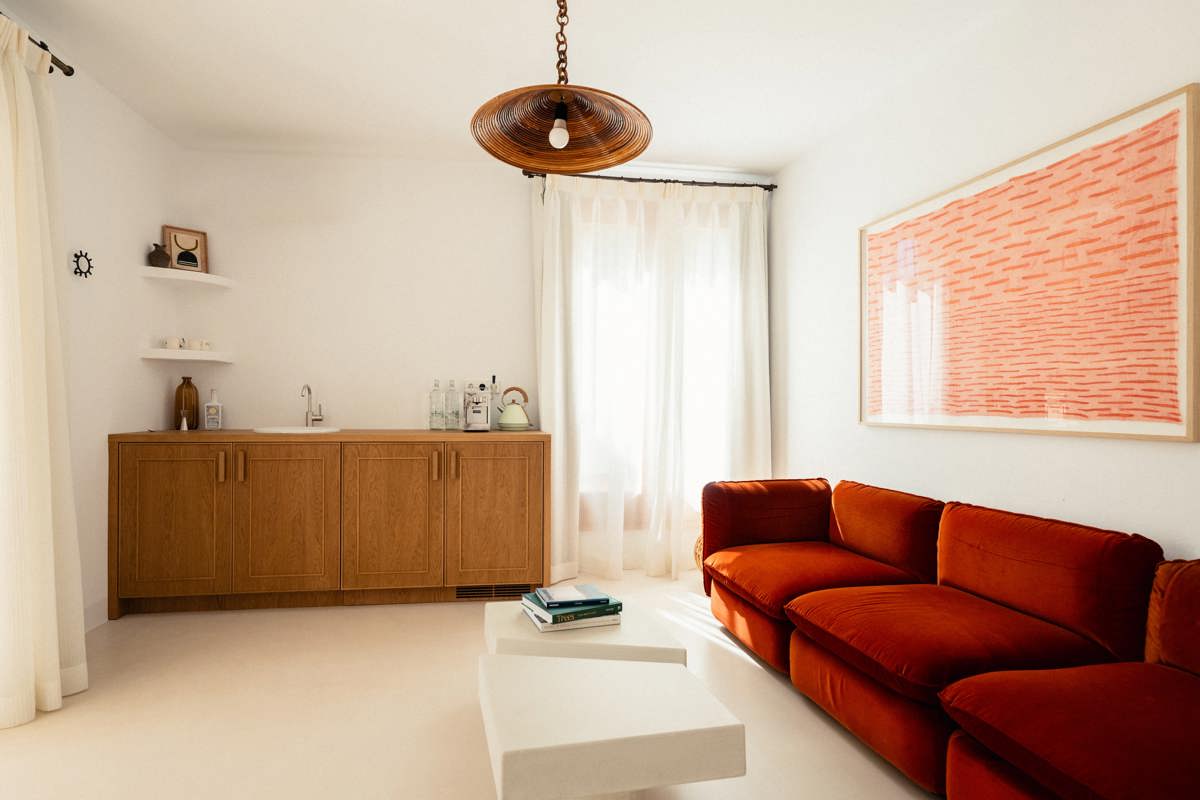 Espace de vie lumineux avec canapé orange brûlé, kitchenette moderne en bois, art abstrait et lumière naturelle.