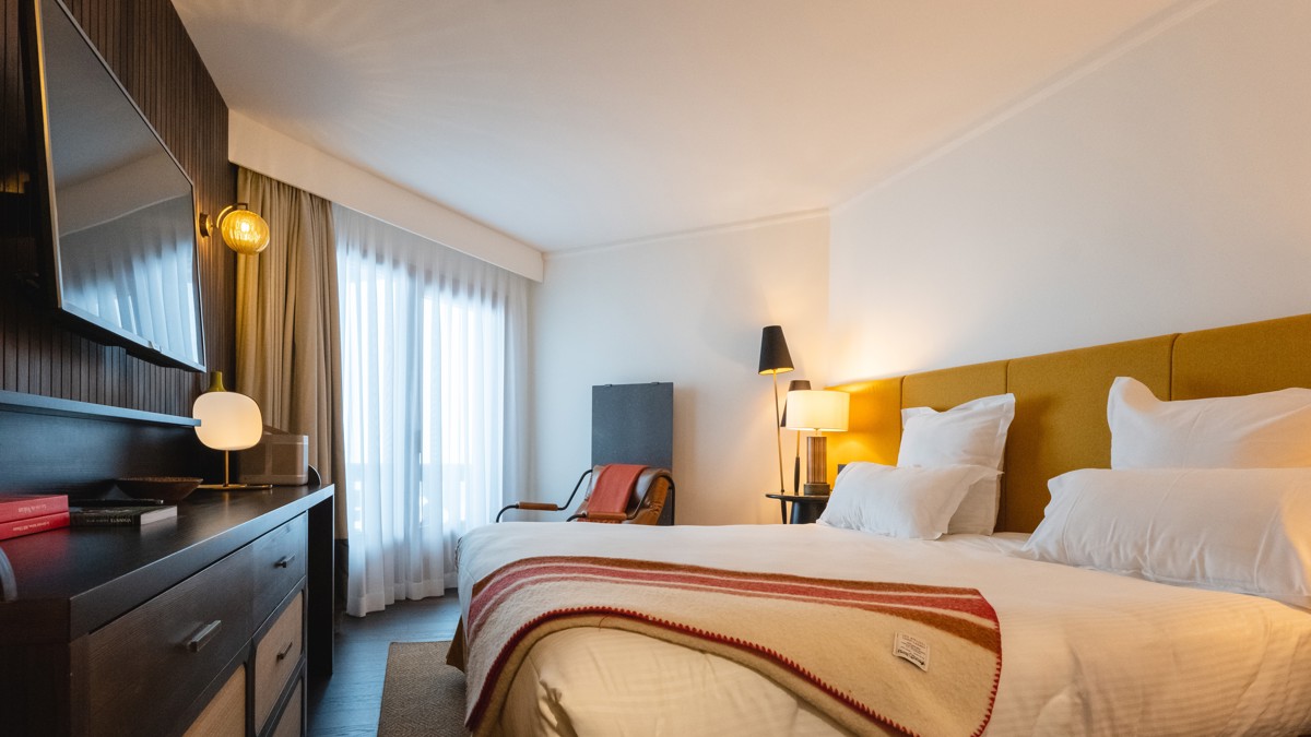 A wall-mounted TV is in front of the bed, with a chair placed beside it.