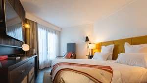 A wall-mounted TV is in front of the bed, with a chair placed beside it.