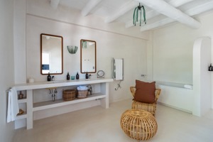Grande salle de bain avec double vasques, fauteuil en osier, décoration minimaliste et lumière naturelle douce.