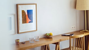 A portrait is mounted above a table holding glasses, a fruit bowl, and a notebook.