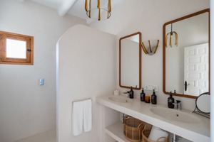 Salle de bain minimaliste avec double vasque, deux miroirs encadrés en bois, paniers en osier et petite fenêtre en bois.