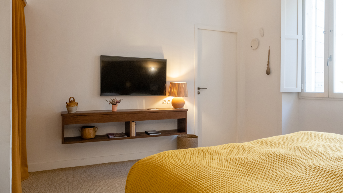 Un téléviseur est fixé au mur au-dessus du meuble, directement face au lit douillet.