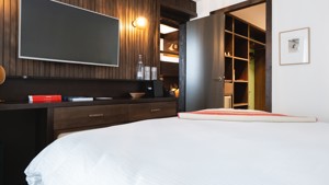 An organized bedroom features a cozy bed with a TV mounted directly in front.