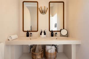 Salle de bain moderne avec deux lavabos, deux miroirs encadrés de bois, des paniers en osier, des distributeurs de savon noirs et une décoration minimaliste dans des tons neutres.